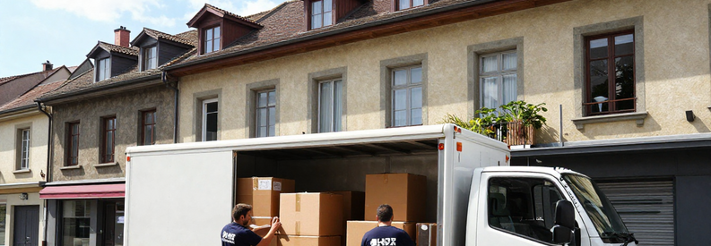 Équipe déménageurs chargeant camion devant immeuble résidentiel bernois, zone urbaine densément peuplée