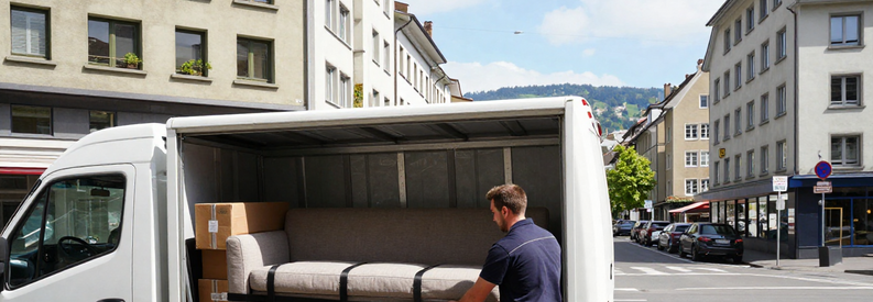 Professionnel chargeant mobilier dans camion devant immeuble zurichois, contexte urbain dense typique canton Zurich