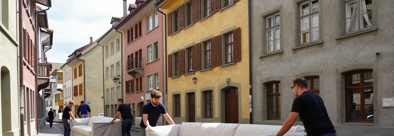 Déménageurs transportant canapé dans ruelle historique étroite Saint-Gall avec façades anciennes typiques