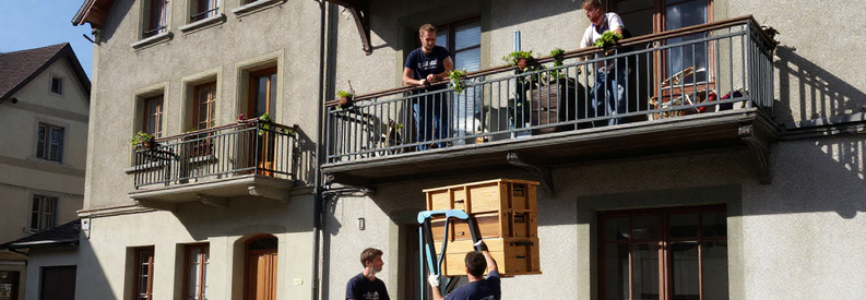 Monte-meuble en action sur façade d'immeuble ancien suisse, déménageurs guidant une armoire au troisième étage