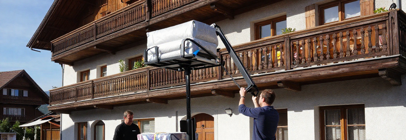 Déménageurs installant un monte-meuble électrique contre façade d'immeuble résidentiel suisse